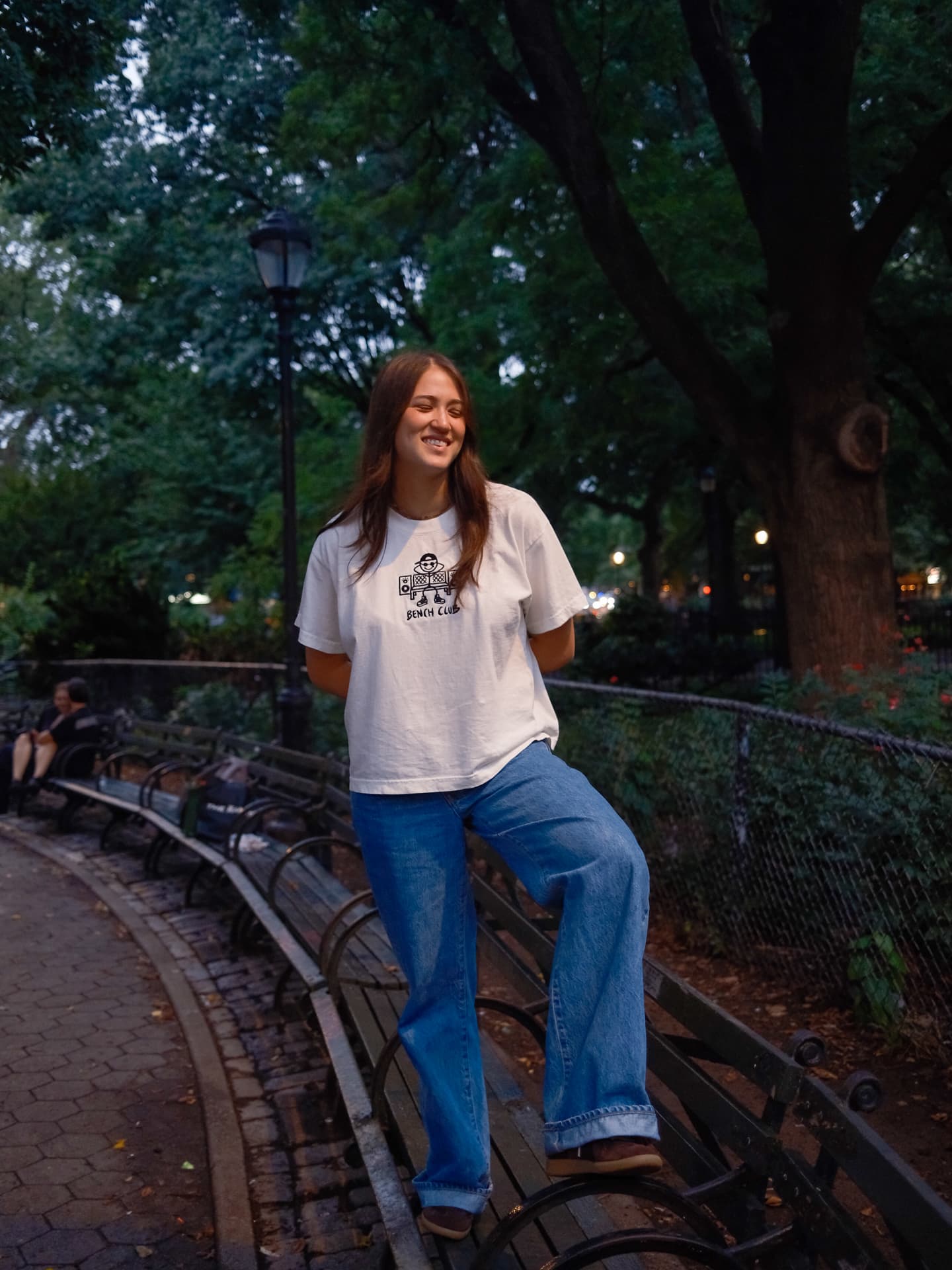 Woman in a white Bench Club tee standing on a park bench