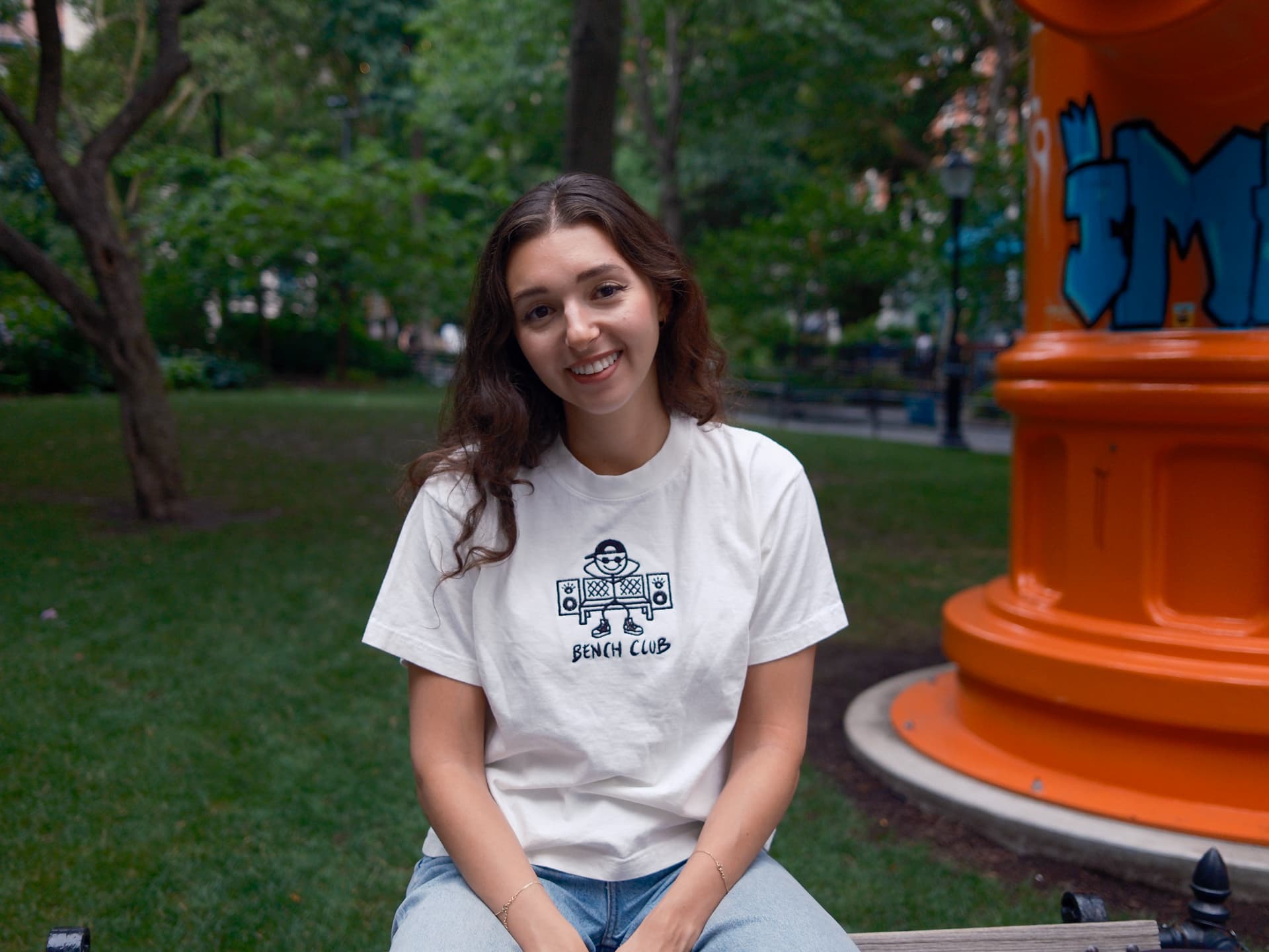 Woman in a white Bench Club tee by an orange hydrant sculpture